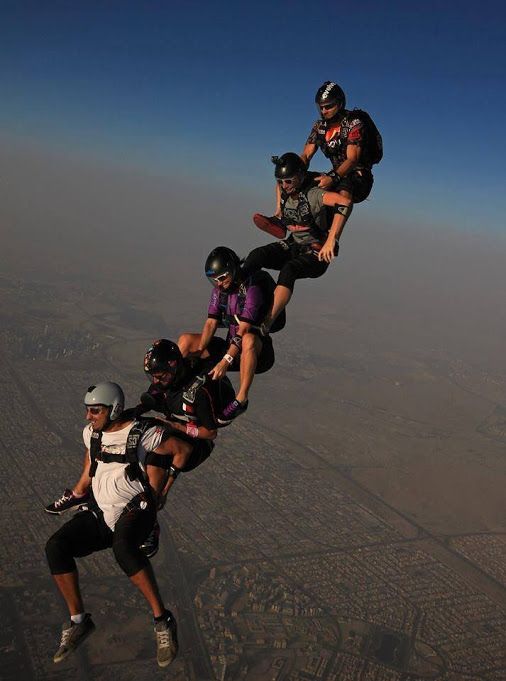 a group of people flying through the air on top of a parachute over a city