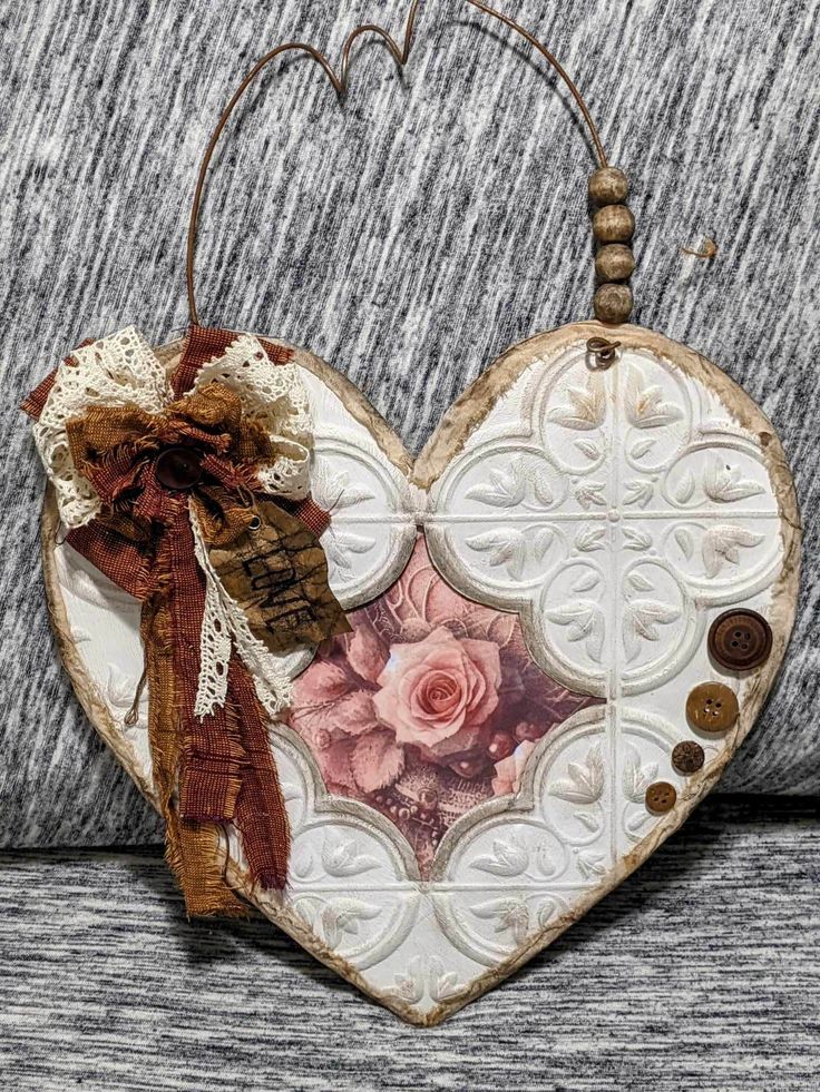 a heart shaped decoration hanging on a wall next to a gray couch with buttons and ribbons