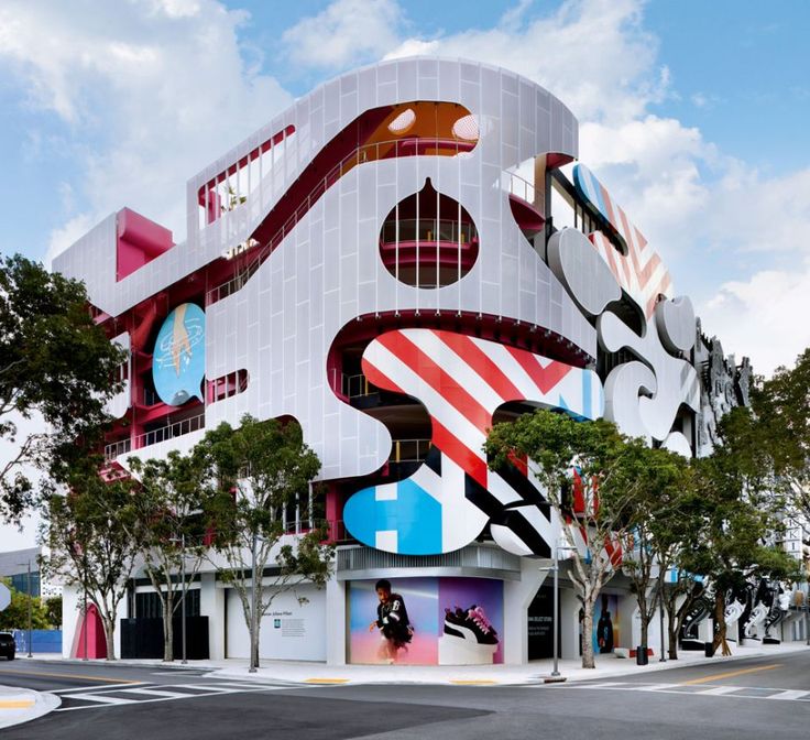 an artistic building with multiple colorful designs on it's side and trees in the foreground