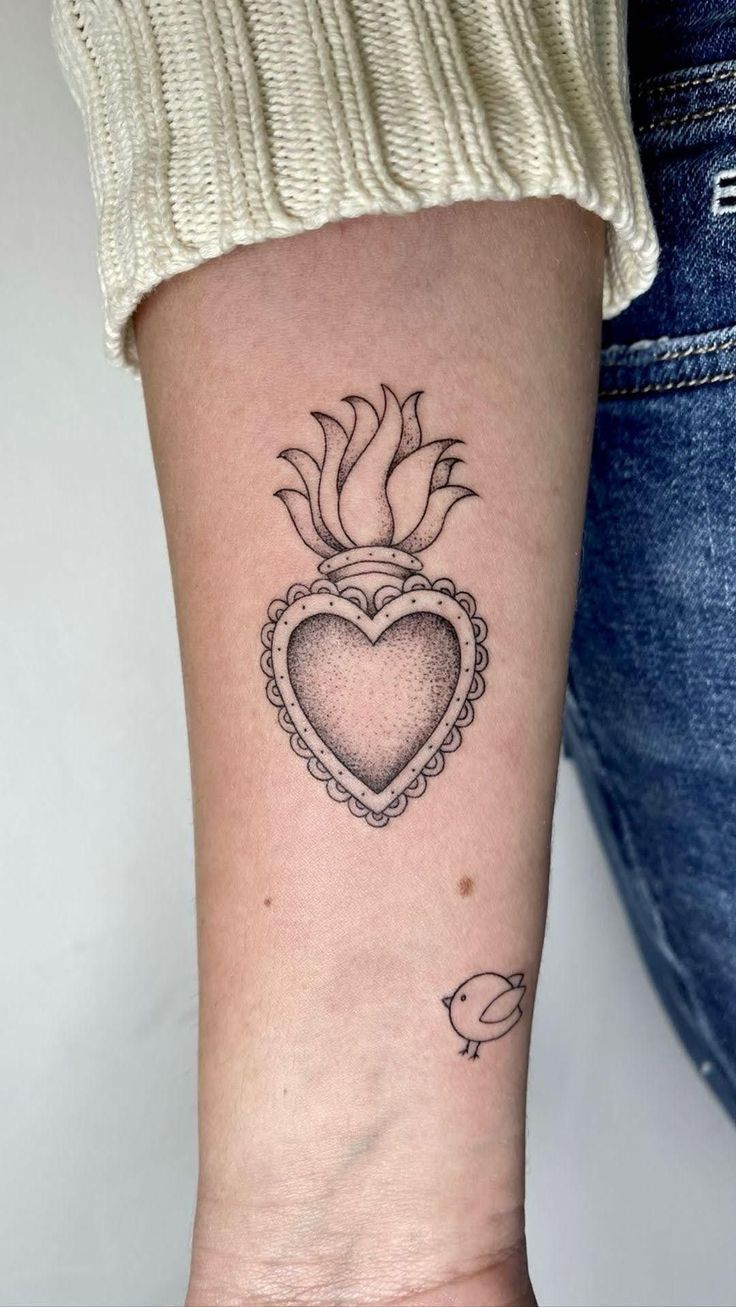 a small heart tattoo on the wrist with an arrow and flower in the center,