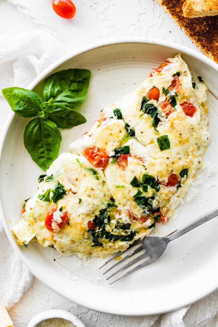 a white plate topped with an omelet covered in cheese and spinach leaves