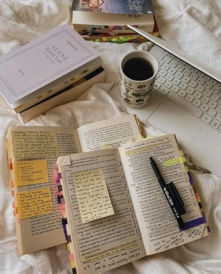 an open book sitting on top of a bed next to a keyboard and cup of coffee