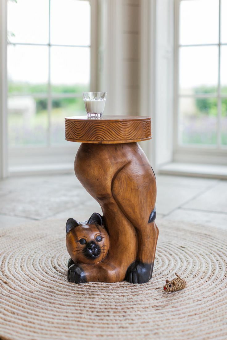 a small wooden cat sitting on top of a table next to a glass cup and saucer