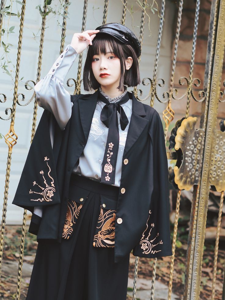 a woman wearing a black outfit and hat standing in front of a gate with chains on it