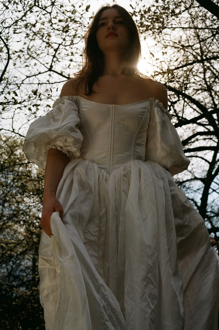 a woman wearing a white dress standing in front of trees