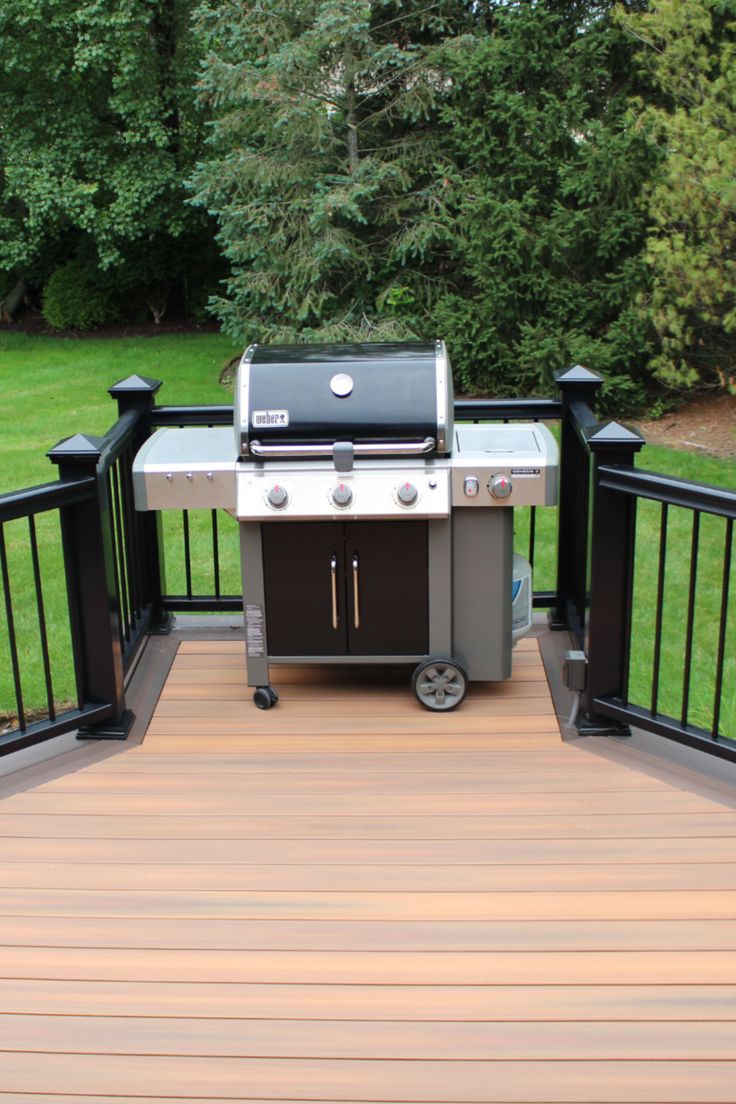 a bbq grill sitting on top of a wooden deck next to a lush green field