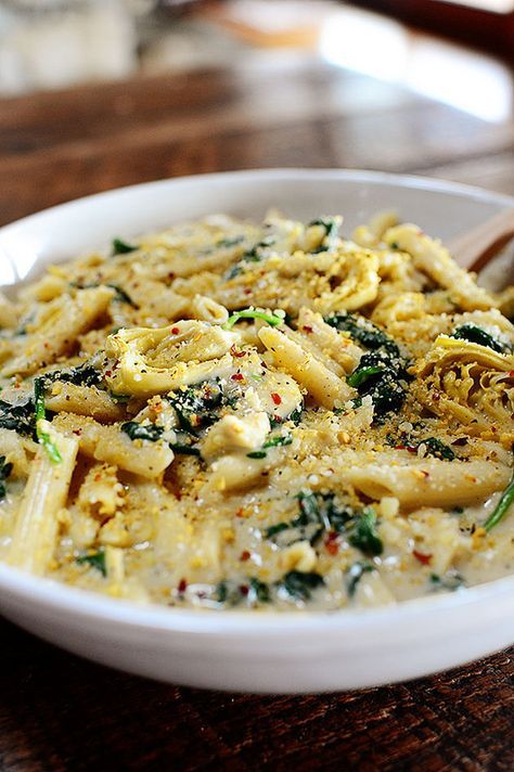 a white bowl filled with pasta and spinach on top of a wooden table next to a fork