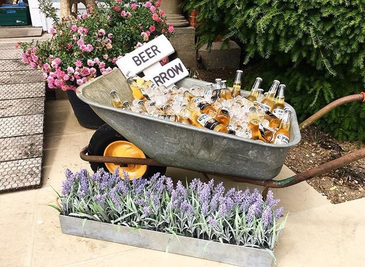 a wheelbarrow filled with bottles of beer sitting next to lavender plants and flowers