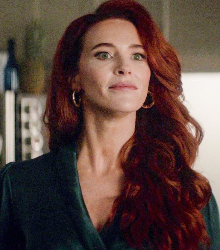 a woman with long red hair standing in front of a kitchen counter and looking off to the side