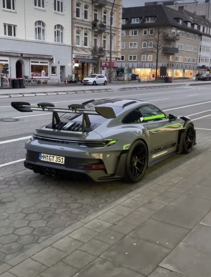 a grey sports car parked on the side of a road next to a city street