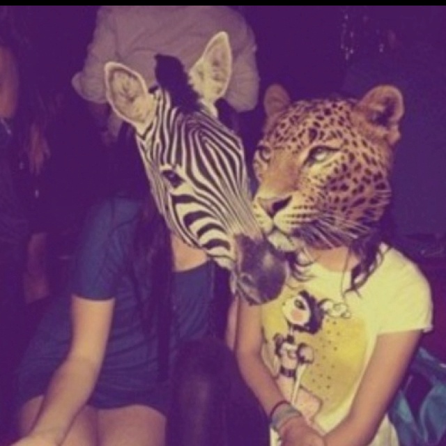 a woman sitting next to a leopard and a zebra mask on her head with other people in the background