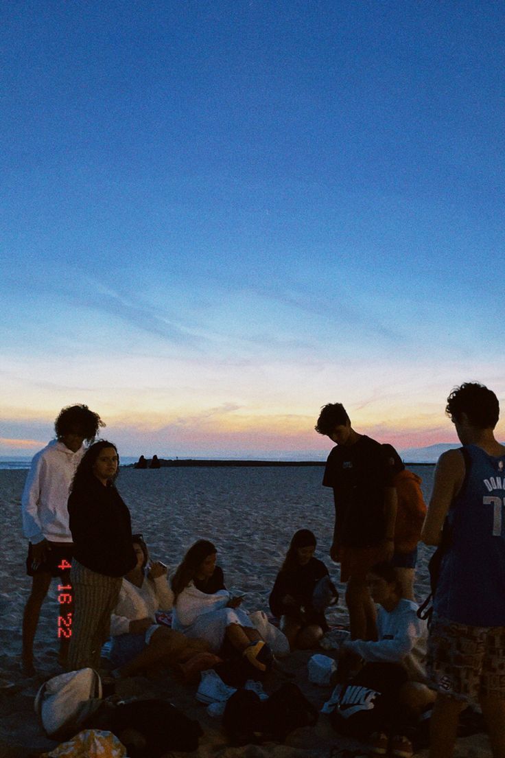 a group of people standing on top of a beach next to the ocean at sunset