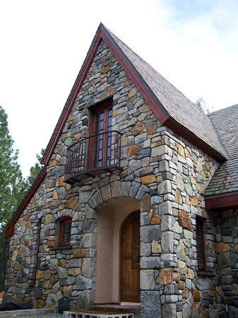 a stone building with a wooden door and window on the front side, surrounded by trees