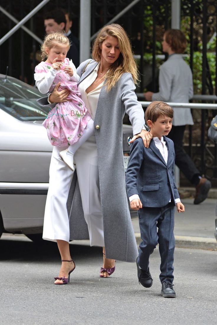 the woman is walking with two children in her arms and she has on a gray coat