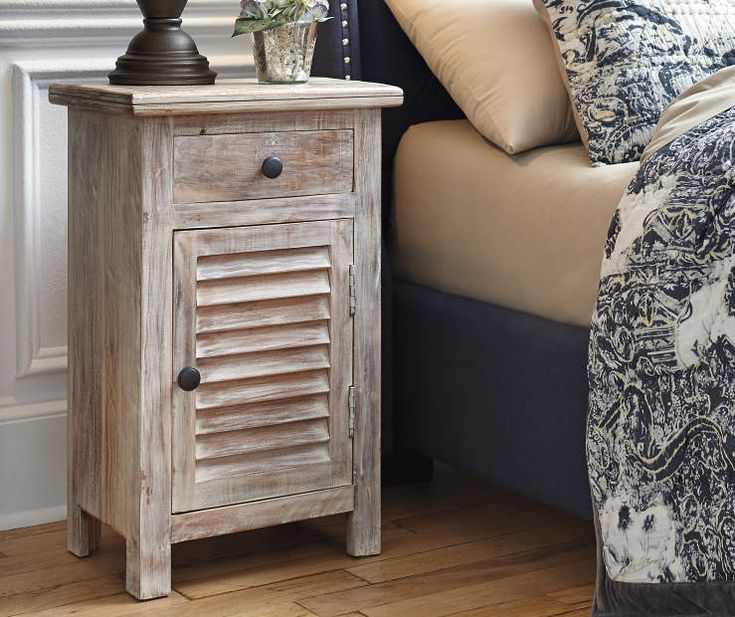 a wooden cabinet next to a bed in a room with white walls and wood flooring