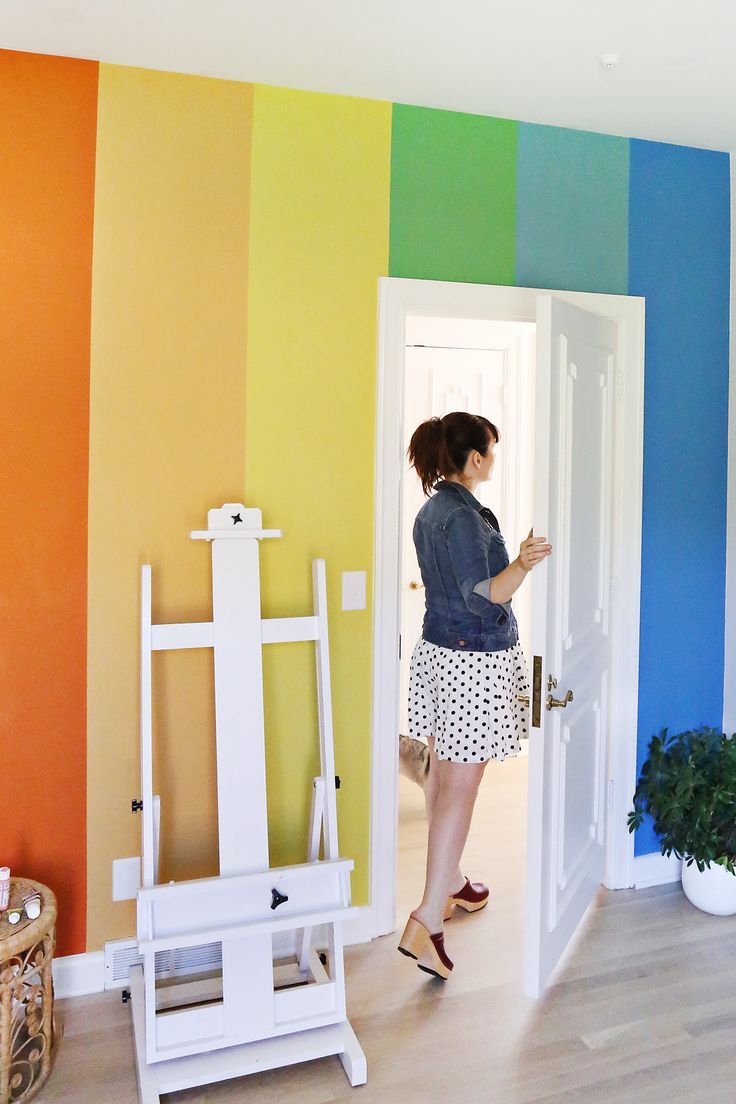 a woman standing in front of a rainbow painted wall