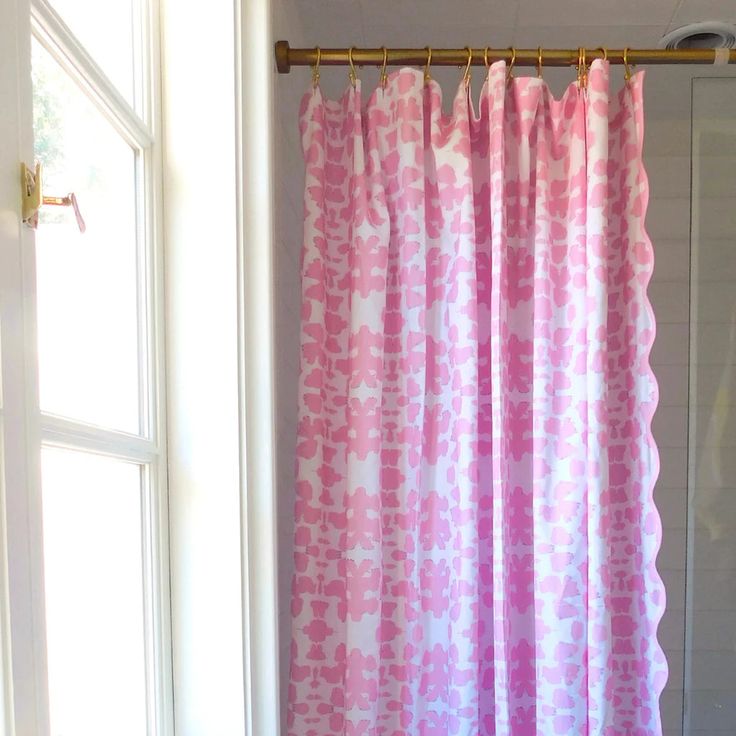 a pink and white shower curtain hanging from a metal rod in front of a window