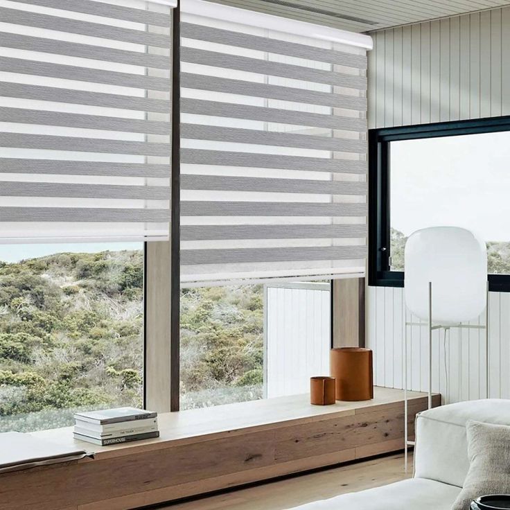 a living room filled with furniture and large windows covered in roman blind shades on top of them