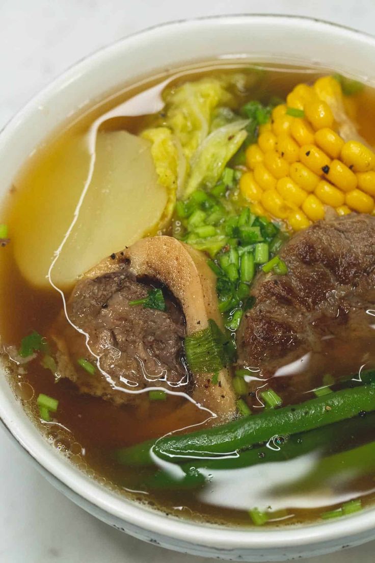 a white bowl filled with meat, vegetables and broth on top of a table