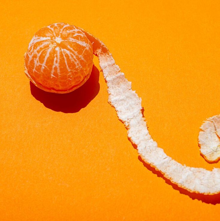 an orange peeled in half with the peel still on it's side, sitting on a yellow surface