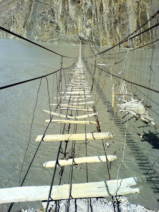 the rope bridge is suspended over water and has many boards attached to each side with ropes