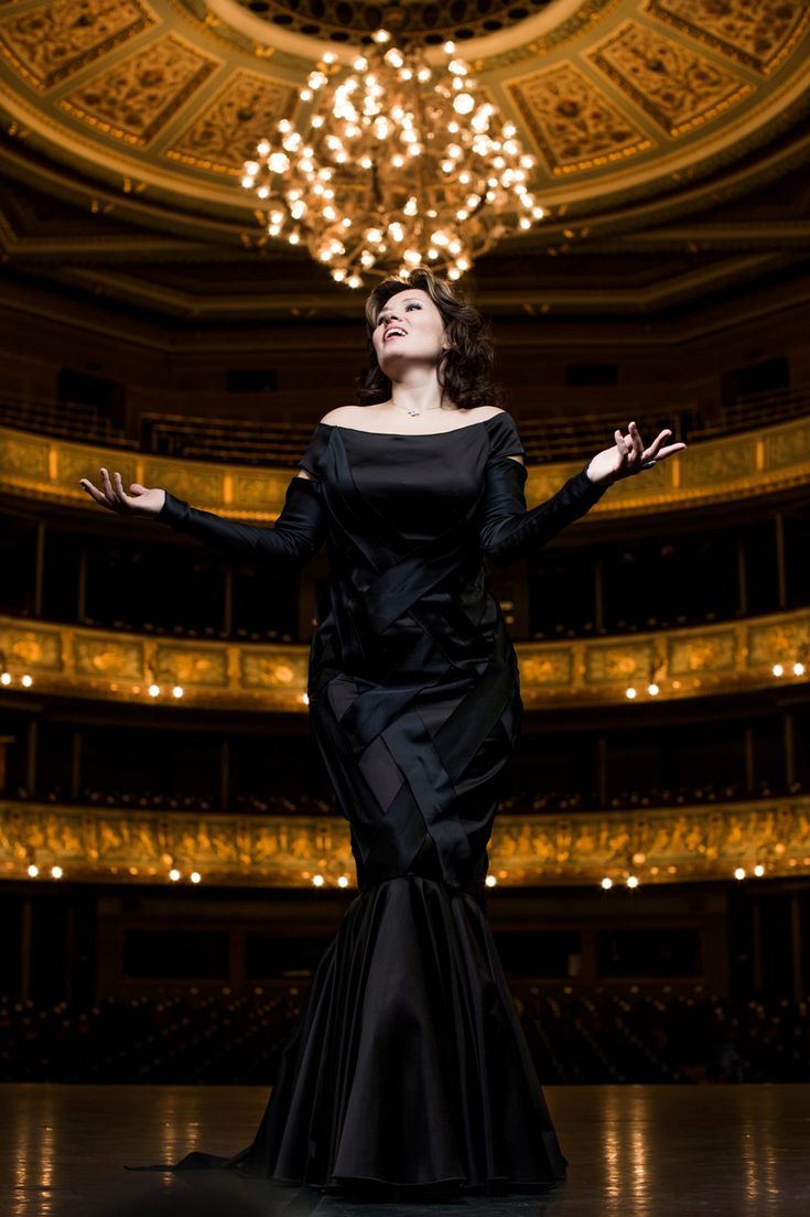 a woman in a long black dress standing on a stage with her arms spread out