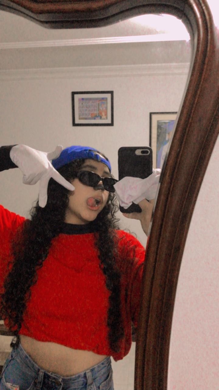 a woman in red shirt and blue hat standing in front of mirror