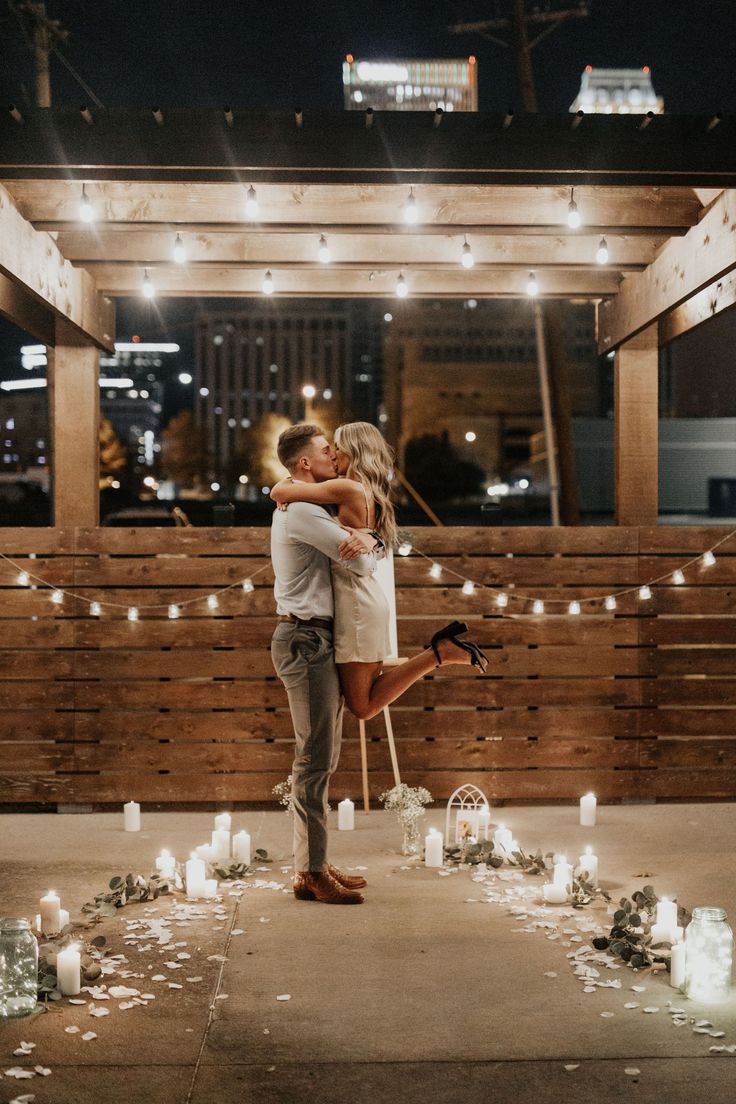 a man and woman kissing in front of candles on the ground with lights strung all around them