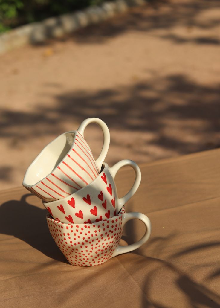 three coffee cups stacked on top of each other with hearts painted on them, sitting on a table