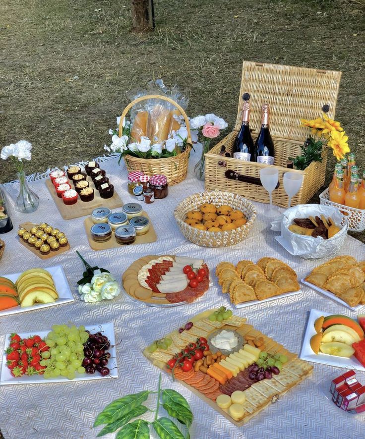 an outdoor picnic with food and drinks on the table in front of it, along with wine bottles