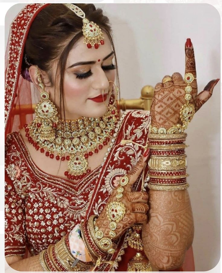 a woman in a red and gold bridal outfit holding her hands up to her face