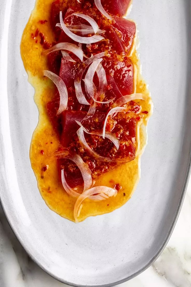 a white plate topped with meat and onions on top of a marble countertop next to a knife