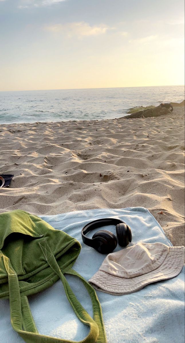 a hat, headphones and towel on a blanket at the beach with water in the background