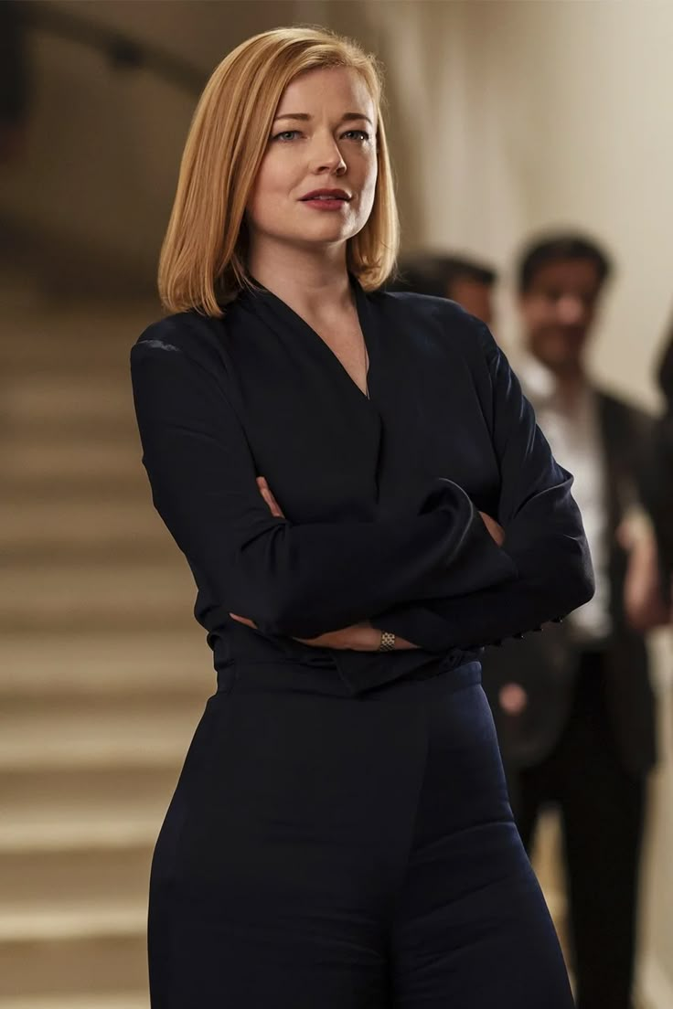 a woman with her arms crossed standing in front of stairs