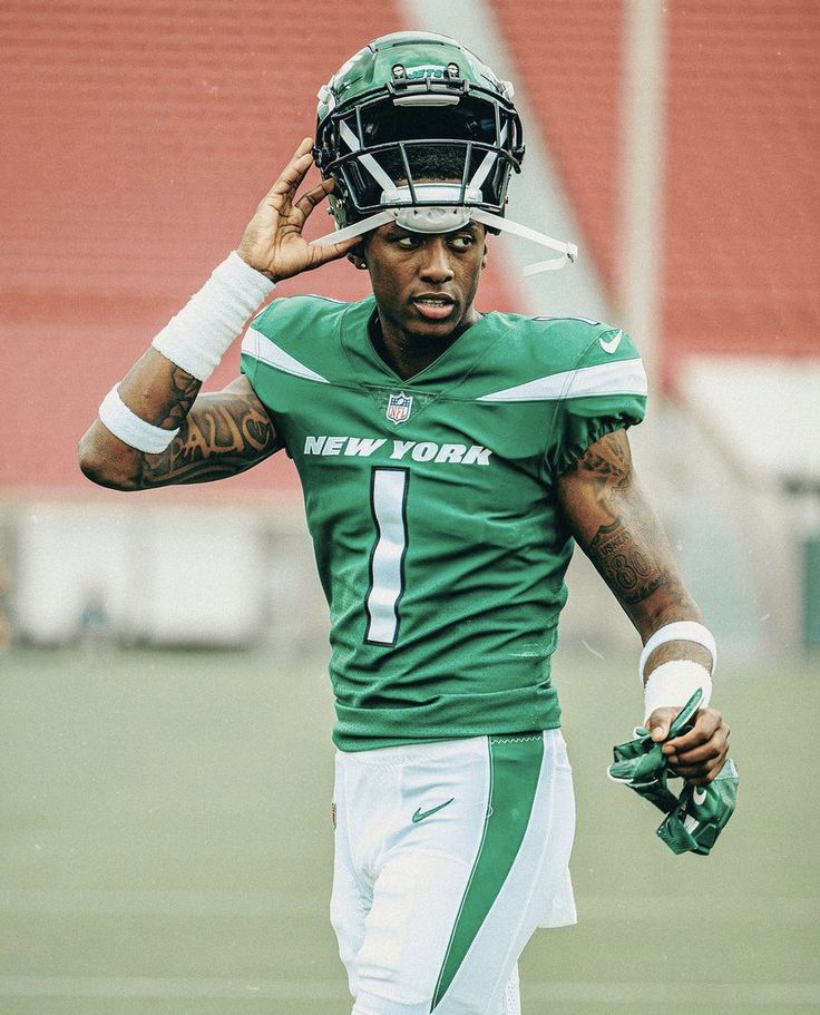 a football player holding his helmet on the sideline during a green and white game