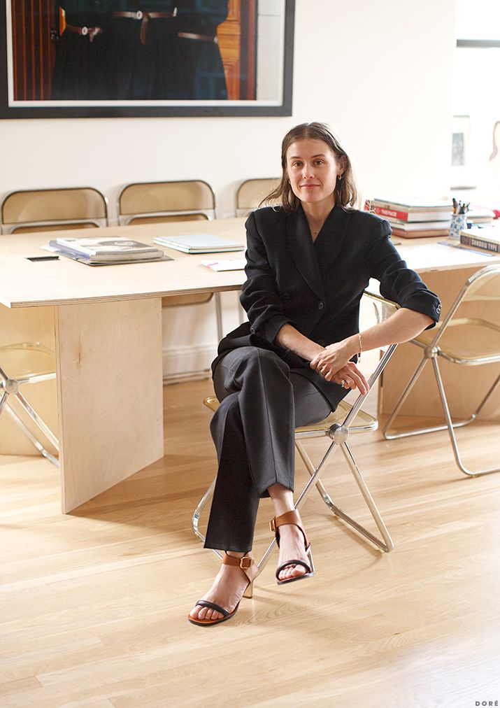 a woman sitting on a chair in front of a table with two chairs and a painting behind her