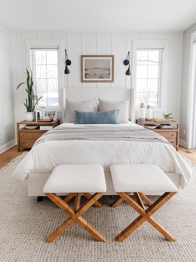 a bedroom with white bedding and two stools in front of the headboard