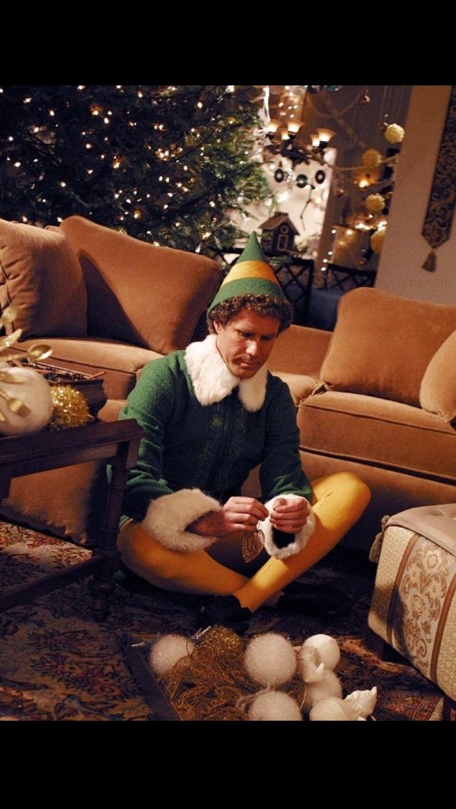 a man sitting on the floor in front of a christmas tree wearing a gnome hat