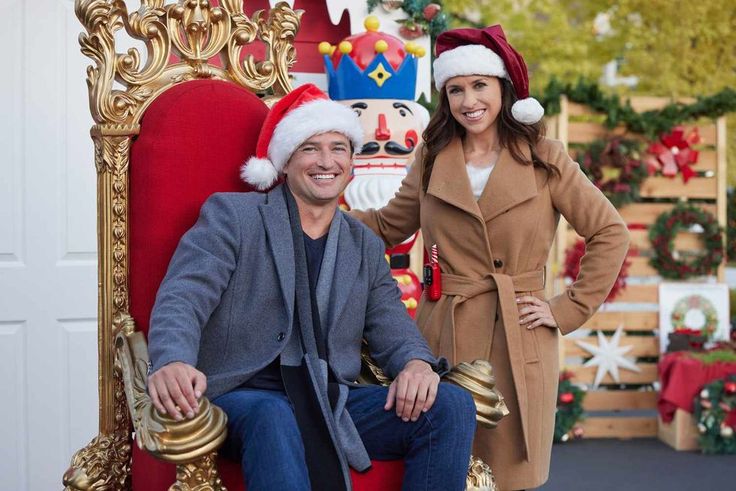 a man and woman in christmas hats sitting on a red chair with gold trimmings