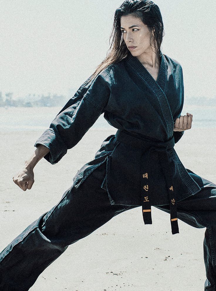 a woman is doing karate on the beach with her arms stretched out and one leg in the air