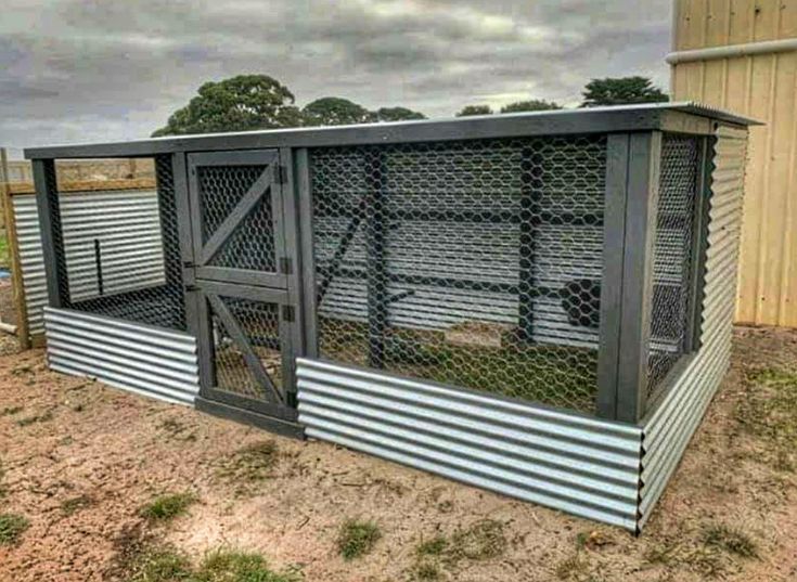 a large metal structure sitting in the middle of a dirt field next to a building