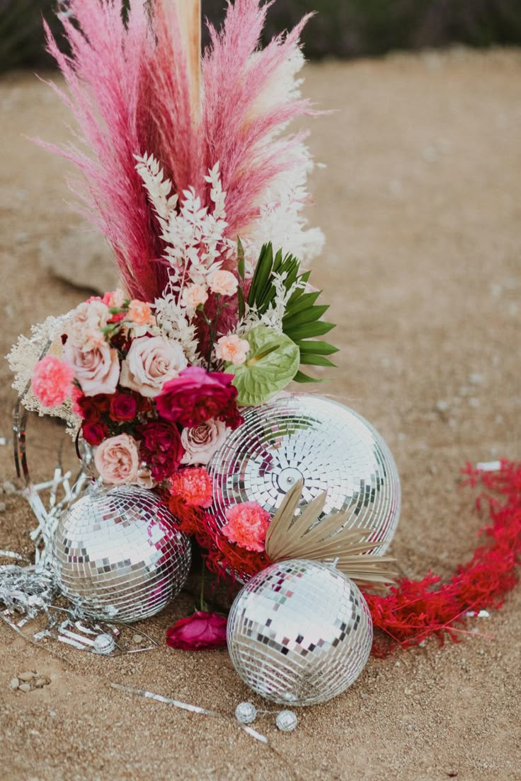 some disco balls and flowers are on the ground with red feathers in it's centerpiece