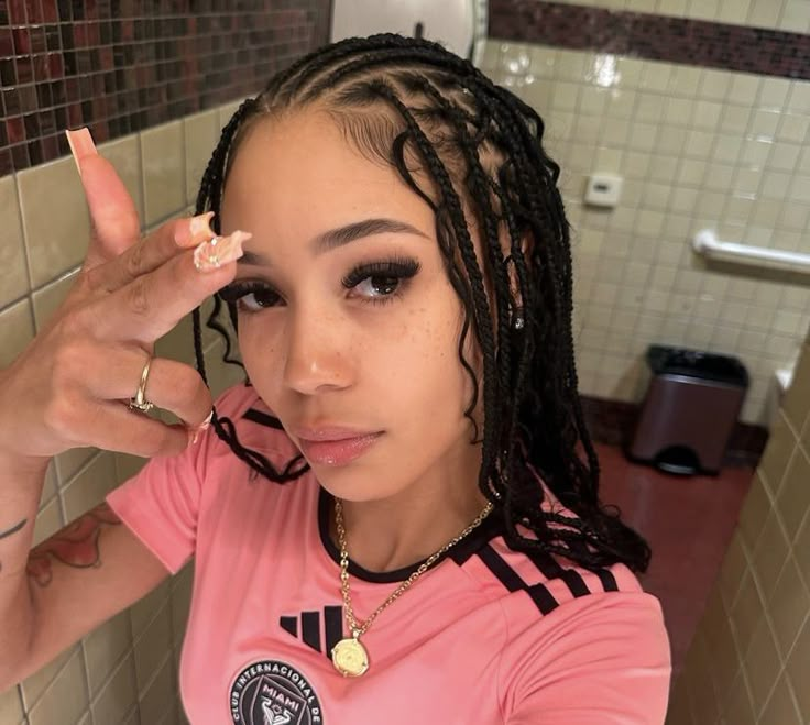 a woman with dreadlocks in a bathroom pointing to the side while wearing a pink shirt