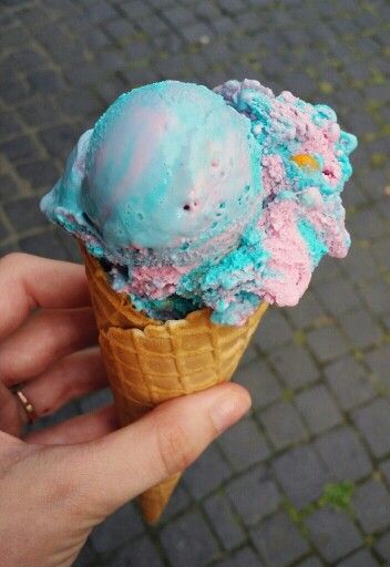 a hand holding an ice cream cone with blue and pink topping