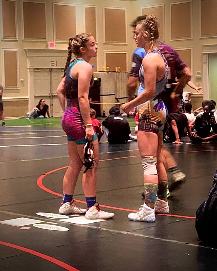 two women standing on top of a wrestling ring with their hands in their pockets and knee pads