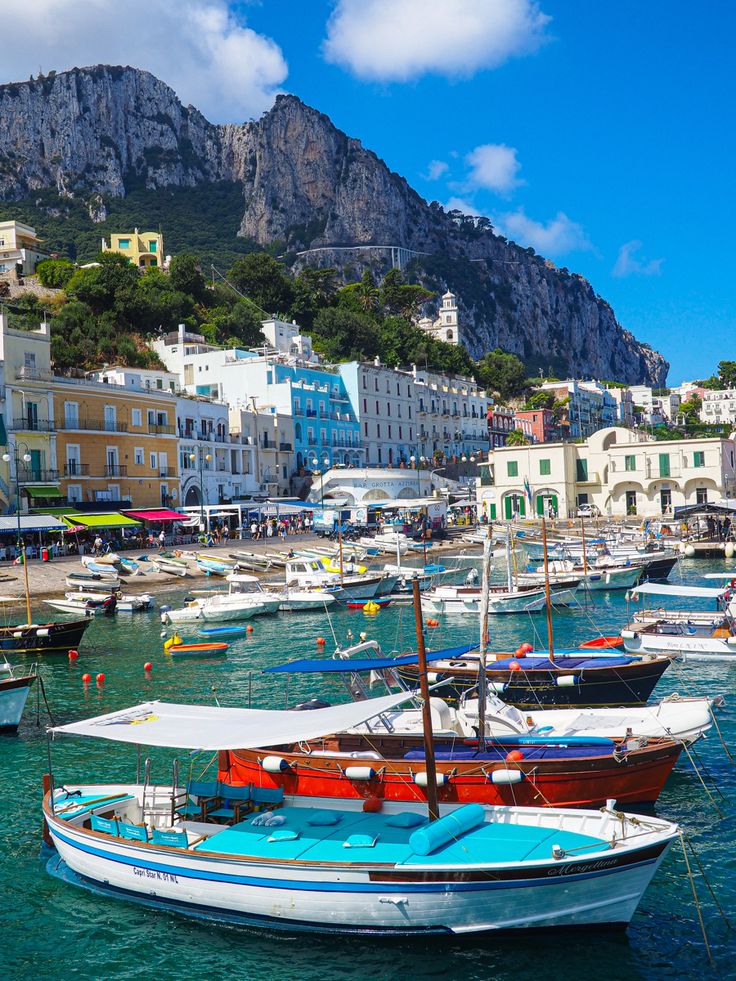 many boats are docked in the water near some buildings and cliffs on a hill side