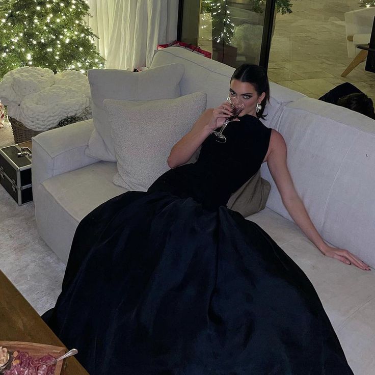 a woman sitting on a couch with a glass of wine in her hand while wearing a black dress