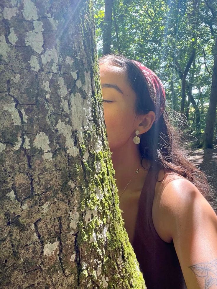 a woman is hiding behind a tree in the woods with her eyes closed and nose covered by moss