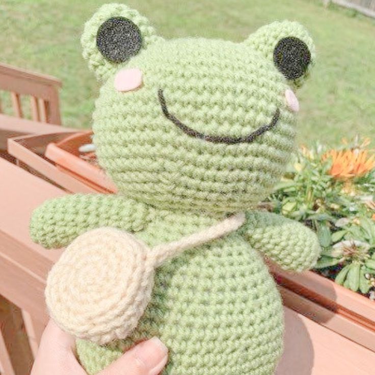 a crocheted frog sitting on top of a bench next to a potted plant