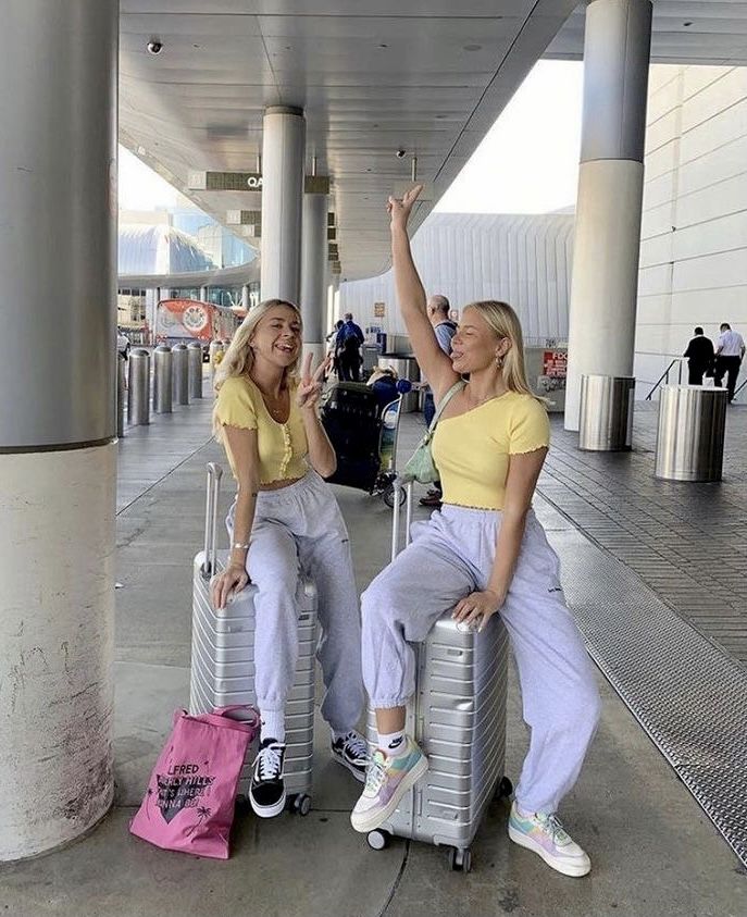 two women sitting on suitcases at an airport with their arms up in the air